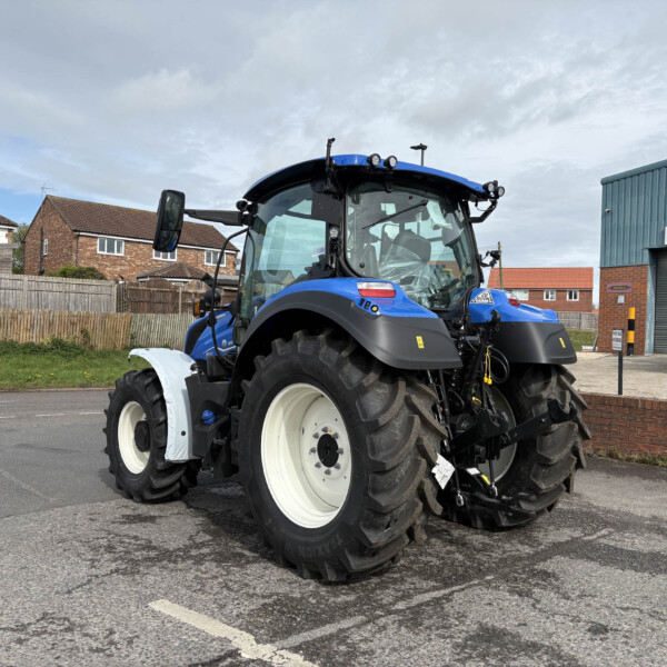 Blue agricultural tractor parked in a paved lot beside a brick building and a shop sign that reads Pöttinger.