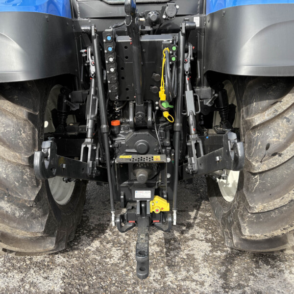 Rear tractor hitch with hydraulic controls between large muddy tires, warning stickers visible on fenders between blue and black bodywork