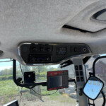 Interior view of a tractor cab with a dashboard, controls, and a mounted display screen near the windshield.