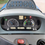 Close-up of a tractor dashboard with analog gauges, a central digital readout, and warning lights above.