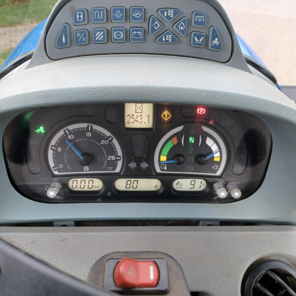Close-up of a tractor dashboard with analog gauges, a central digital readout, and warning lights above.