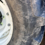 Close-up of a dirty tractor tire showing rugged tread and a white wheel rim with bolts.