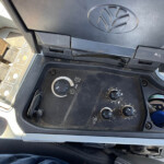 Open car fuse panel with color-coded fuses and nearby dashboard controls visible