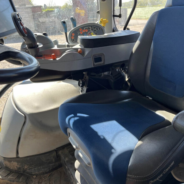Interior of a tractor cab with a blue driver seat, steering wheel, and a console full of colorful buttons and a screen.