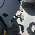 Interior of a dusty heavy equipment cab showing three textured metal foot pedals and a dirt-streaked floor.