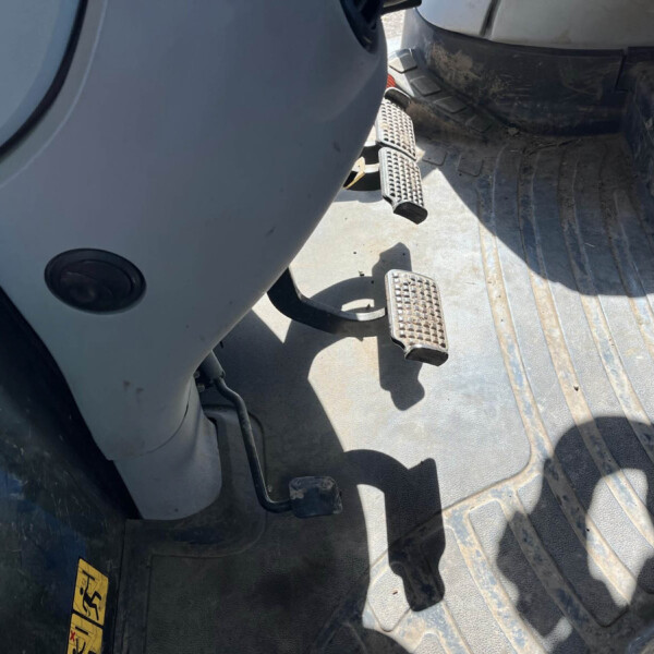 Interior of a dusty heavy equipment cab showing three textured metal foot pedals and a dirt-streaked floor.