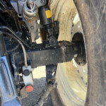 Close-up of a truck trailer suspension area showing a black hydraulic damper and metal linkage next to a dirty, mud-splattered wheel rim.