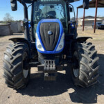 Front view of a blue agricultural tractor with oversized tires, parked on a gravel lot; 'RUSSELLS' branding on the cab windshield