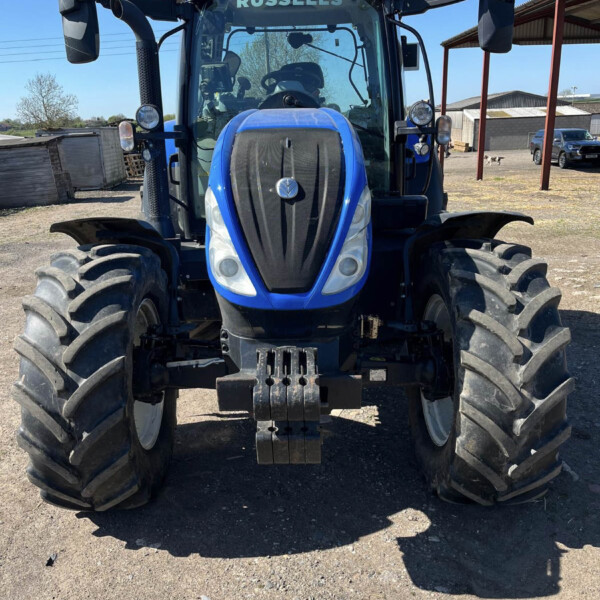 Front view of a blue agricultural tractor with oversized tires, parked on a gravel lot; 'RUSSELLS' branding on the cab windshield