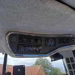 Interior of a vehicle cab showing overhead console with climate knobs, radio, and a blue tractor decal on the panel