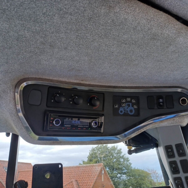 Interior of a vehicle cab showing overhead console with climate knobs, radio, and a blue tractor decal on the panel