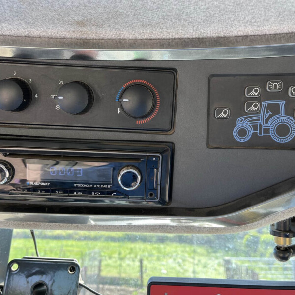 Dashboard of a tractor cabin with climate control dials, a Blaupunkt radio, and a panel featuring a blue tractor graphic on the right