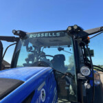 Front view of a blue tractor cab with the word 'RUSSELLS' on the windshield and extra cab lights above the glass.