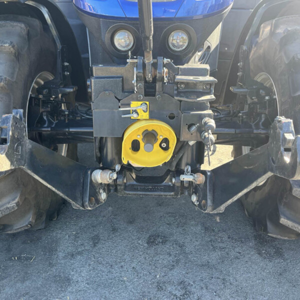 Close-up of a blue tractor front with hitch, hydraulic components, and a bright yellow PTO cover between two large tires.