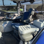 Interior of a heavy machinery vehicle cabin with a large steering wheel, control panel, and blue driver's seat.