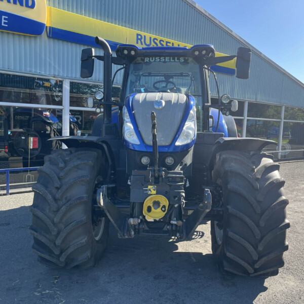 Blue agricultural tractor with oversized tires parked outside a farm equipment dealership under a Russell sign.
