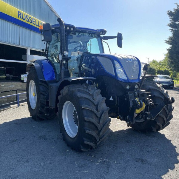 Blue agricultural tractor parked outside a dealership with a yellow-and-blue Russell sign on the building.