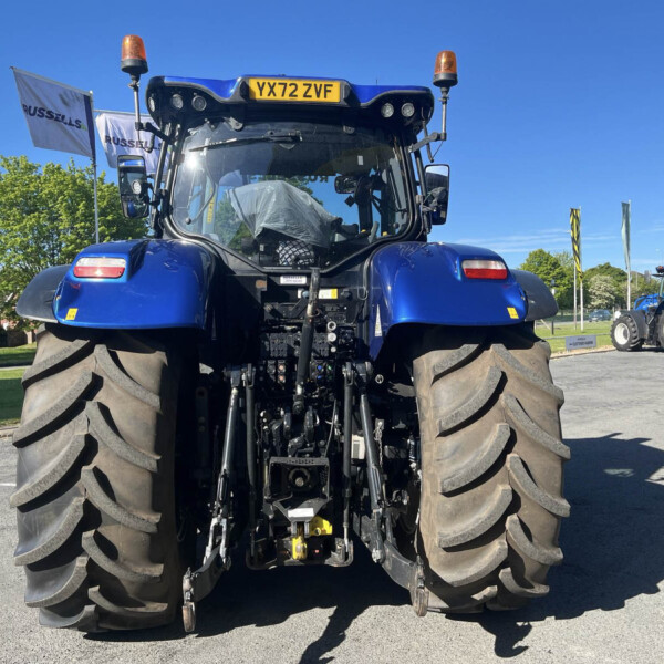 Rear view of a large blue tractor with oversized tires on display, license plate YX72 ZVF, and flags in the background.
