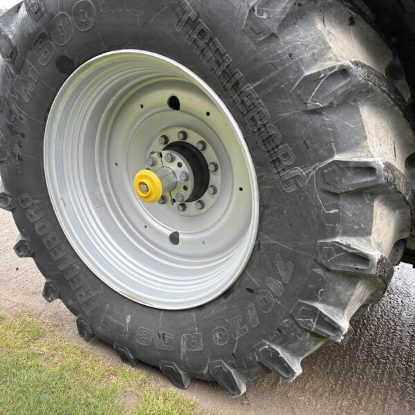 Close-up of a large tractor tire with deep tread and a light gray rim on a dirt surface near grass.
