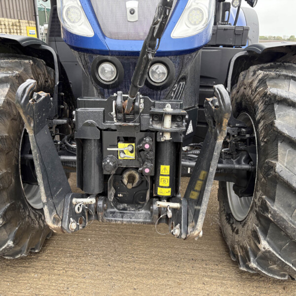 Front view of a blue agricultural tractor showing the heavy hitch, hydraulic linkages, and large treaded tires between the axle wheels.