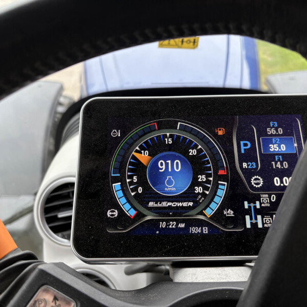 Digital vehicle instrument cluster viewed through the steering wheel, showing RPM around 910 and blue accent gauges