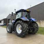 Blue agricultural tractor with oversized tires parked outside a gray industrial building.