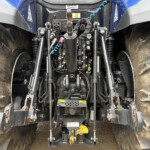 Close-up view of a tractor's rear hitch area with hydraulic levers, control knobs, and hoses between muddy, oversized tires.