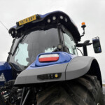 Blue New Holland tractor front, with a yellow UK license plate reading 'YK74 XWY' mounted on the cab top, and large tires visible below.