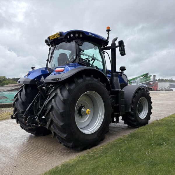 Blue agricultural tractor with oversized tires parked on a concrete lot beneath a cloudy sky.