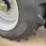 Close-up of a large tractor wheel with a yellow hub cap and multiple lug bolts, mounted on a gray rim on dirt ground.