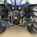 Front view of a blue tractor showing a central hitch assembly between two large, muddy tires and exposed hydraulic components in the lower front.