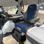 Interior of a heavy machinery cab showing a blue-gray driver seat and a mounted touchscreen tablet to the left of the steering wheel.