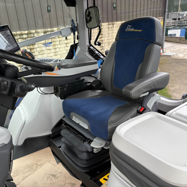 Interior of a heavy machinery cab showing a blue-gray driver seat and a mounted touchscreen tablet to the left of the steering wheel.