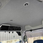 Interior view of a truck cab ceiling with overhead console and speaker, windshield and outside building visible out the window.