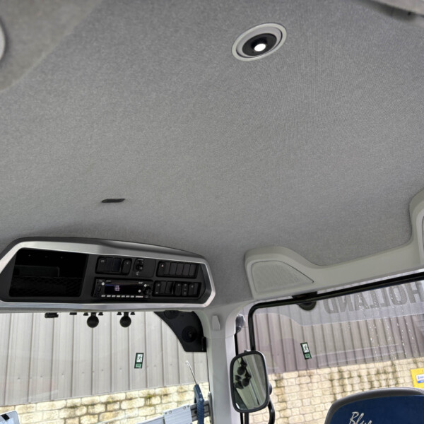 Interior view of a truck cab ceiling with overhead console and speaker, windshield and outside building visible out the window.