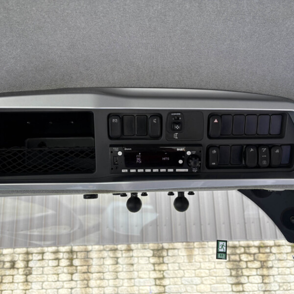 Close-up of a vehicle dashboard showing the radio, buttons, and vents, with a textured headliner above and a stone wall visible through the windshield.