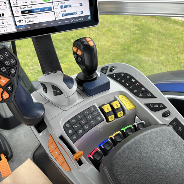 Interior of a tractor cab with a joystick and multicolor control panel buttons and a touchscreen display.