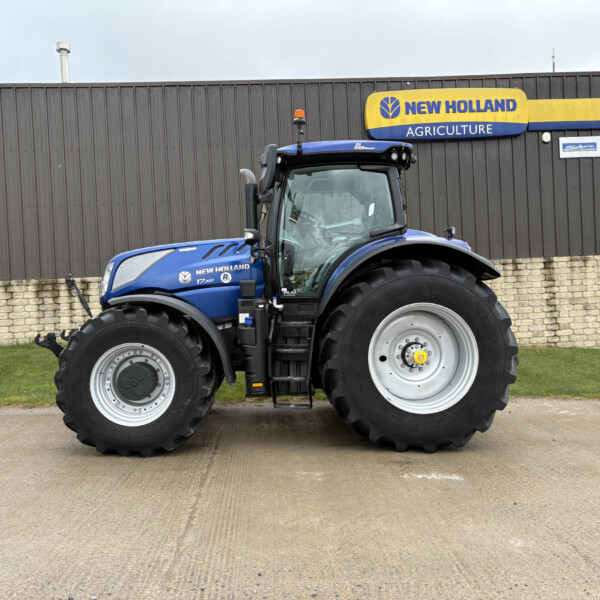 Blue New Holland tractor parked in front of a gray metal building with a yellow sign reading New Holland Agriculture.