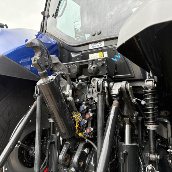 Close-up of a blue tractor front with exposed hydraulic components and suspension arms.