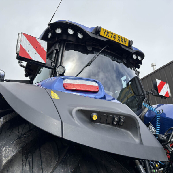 Close-up of a blue tractor front with a yellow license plate reading YX74 XXH and roof lights.