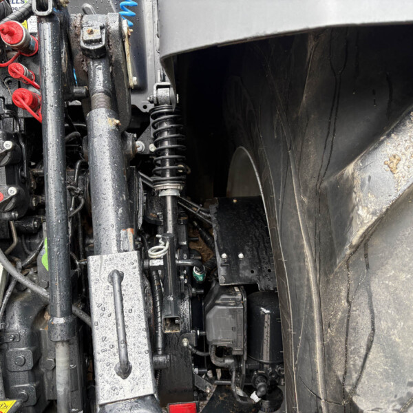 Close-up of exposed hydraulic system and wiring on heavy machinery, showing red caps, blue components, and damp surfaces near a large tire edge.