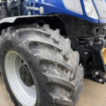 Close-up of a large muddy tractor rear tire on a blue New Holland tractor, showing tread and wheel rim detail.