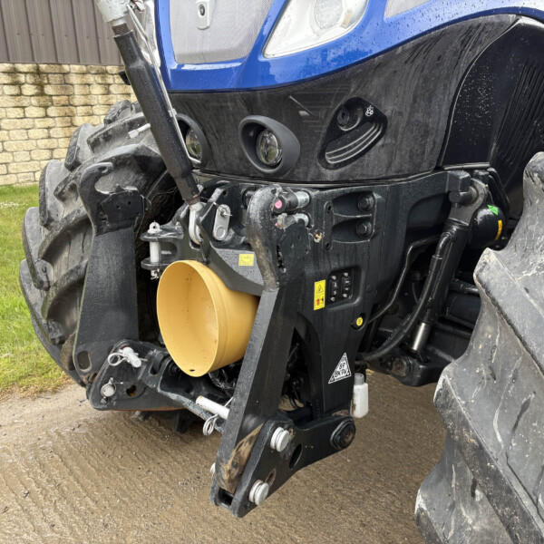 Close-up of a blue tractor's front end showing muddy tires, hydraulic linkages, and a yellow circular shield/opening.