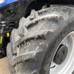 Close-up of a muddy tractor front wheel and fender, showing a large tire and dirt splatter on the body.