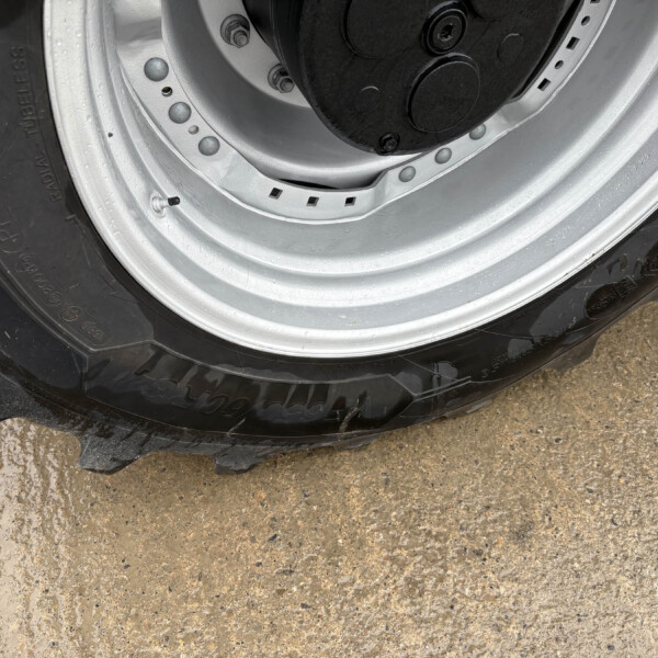 Close-up of a car wheel: black tire with a silver rim, showing the valve stem and lug area on a muddy surface.
