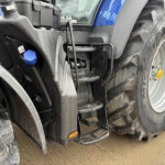 Close-up of a blue tractor showing muddy tire, front steps, hydraulic components and a blue cap.