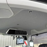 Interior of a truck cab with a mounted tablet screen, overhead console, and grey fabric headliner visible by the windshield and mirrors