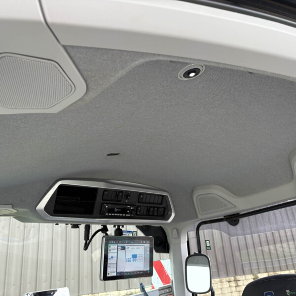 Interior of a truck cab with a mounted tablet screen, overhead console, and grey fabric headliner visible by the windshield and mirrors