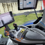 Cockpit of a heavy-duty vehicle with multiple mounted tablet screens showing control interfaces and a joystick within the cab.