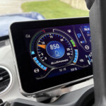 Close-up of a car's digital instrument cluster showing speed/RPM gauges with blue accents and a bluePower label on the screen inside the vehicle interior.